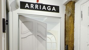A hallway with a white door labeled "ARRIAGA," a wooden door with a textured surface, and a white wall with a window. - Pensión Lo Bilbao (Bilbao)