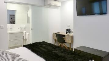 Ett modernt hotellrum med en säng, ett skrivbord, en stol, en TV och en luftkonditioneringsanläggning.