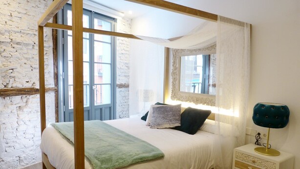 A four-poster bed with a white canopy, a bedside table with a lamp, and a mirror above the bed. - Pensión Lo Bilbao (Bilbao)