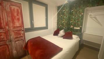 Een slaapkamer met een bed, een rode deken, een wit kussen, een rood kussen, een witte nachtkastje en een garderobe.