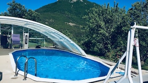 Ein Schwimmbecken mit Glasveranda, Sprungbrett und Bergblick im Hintergrund.