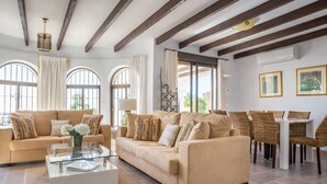Un ampio soggiorno con un divano color beige, un tavolino in vetro e un'area pranzo con sedie in vimini.