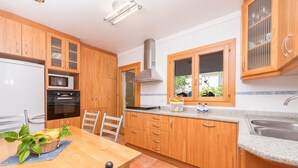A kitchen with wooden cabinets, a microwave, an oven, a sink, and a dining table with chairs. - LLAC GRAN - Chalet with terrace in Port d'Alcudia. Free WiFi (Port d´Alcudia)