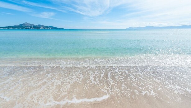 A beach with clear turquoise water, gentle waves, and a distant mountain range. - LLAC GRAN - Chalet with terrace in Port d'Alcudia. Free WiFi (Port d´Alcudia)