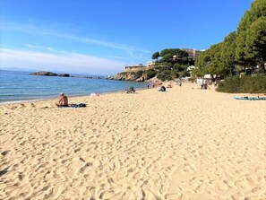 A sandy beach with footprints, a few people, and a building with trees on a hill in the background. - Top flat with every comfort for 1-2 persons, private pool, fibre optic internet (Roses)