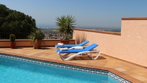 A rooftop pool area with two sun loungers and potted plants.