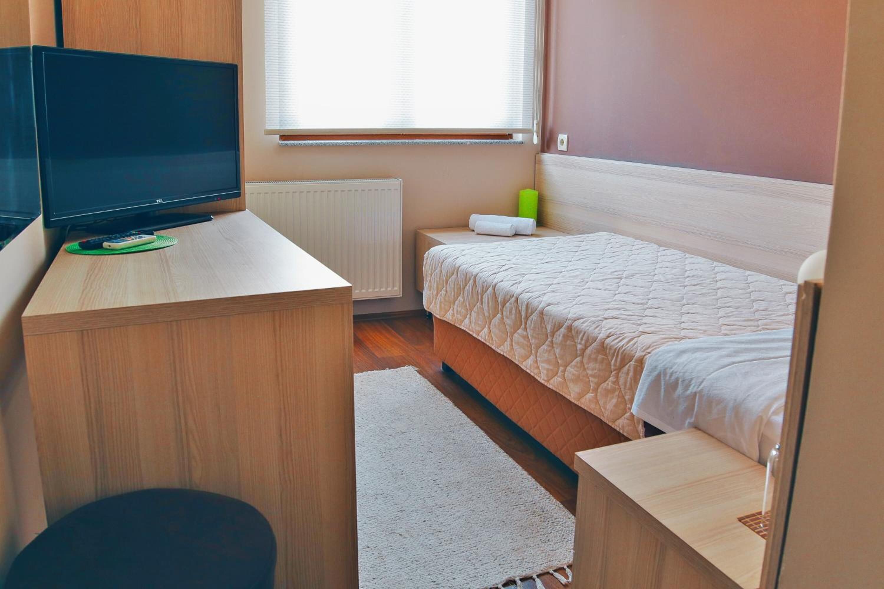 Un dormitorio con cama, escritorio con televisor, radiador y ventana con persianas.