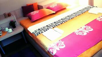 Cama bem arrumada com colcha estampada, travesseiros e mesa de cabeceira com abajur e uma pequena planta.
