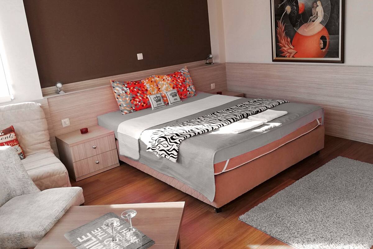 A modern bedroom with a bed, a nightstand, a chair, and a painting on the wall.