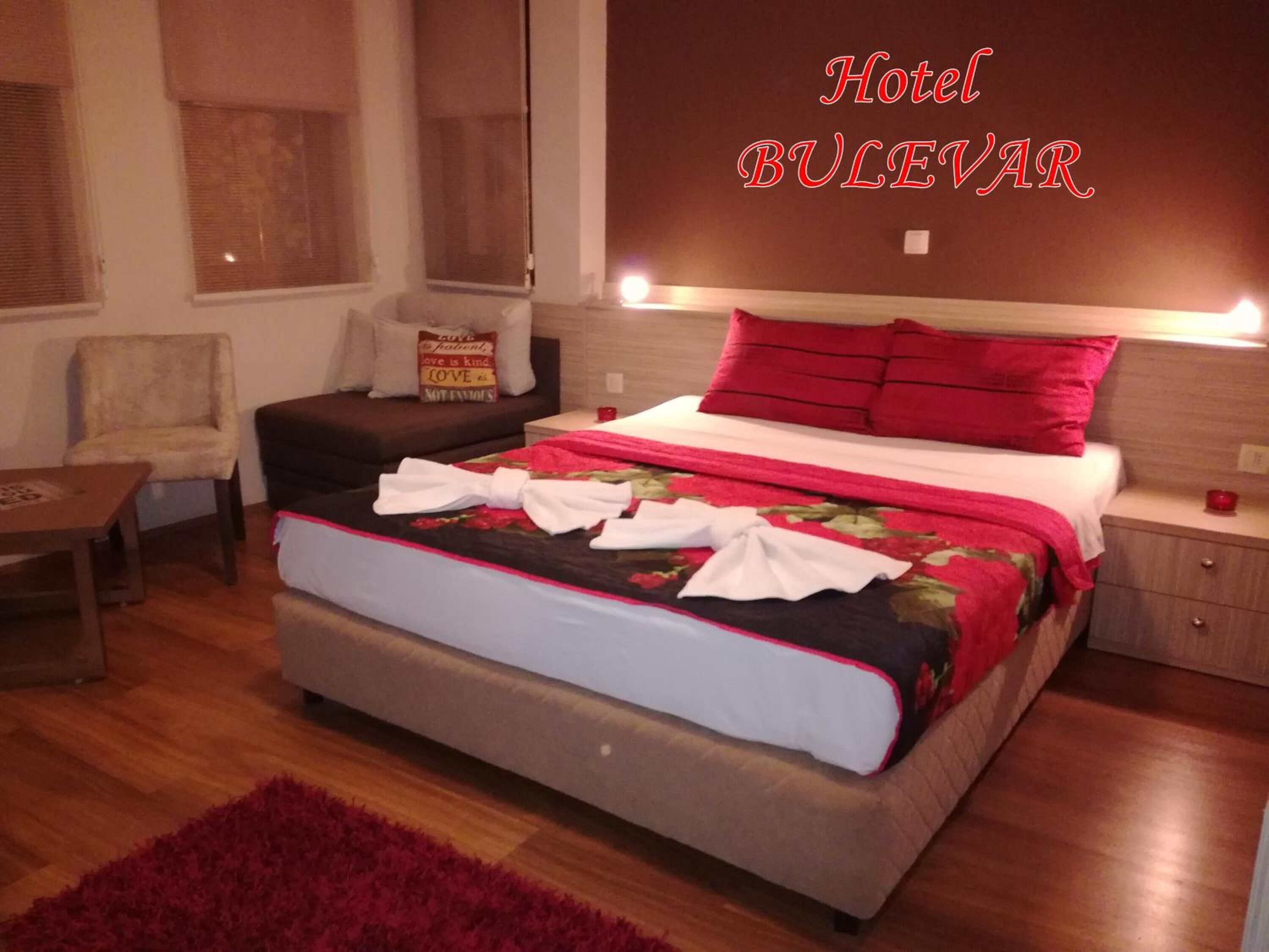 A hotel room with a bed, a chair, a nightstand, and a red rug.
