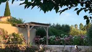 A garden with a pergola, flowering plants, and a stone wall. - Beautiful new villa with garden and pool between vineyards and scrubland (Argilliers)