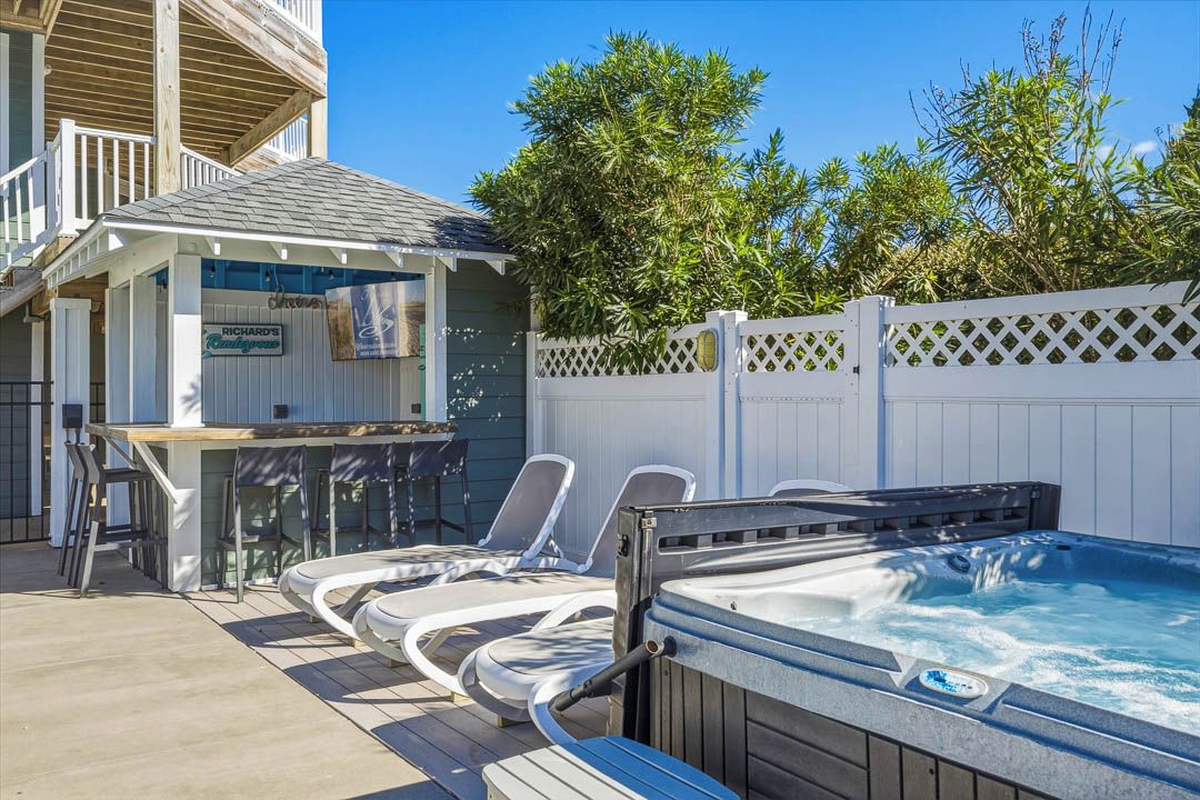 Un bain à remous avec des chaises longues, un coin bar et une terrasse en bois.