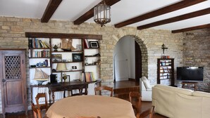 A cozy living room with a stone wall, wooden furniture, a bookshelf, a television, and a dining area. - Villa with private pool, sea view and beautiful beaches within walking distance. (Sarzeau)