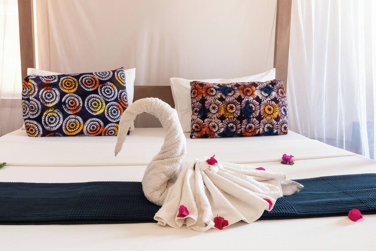 Una cama con dos almohadas estampadas, una toalla decorativa con forma de cisne y una colcha azul oscuro.