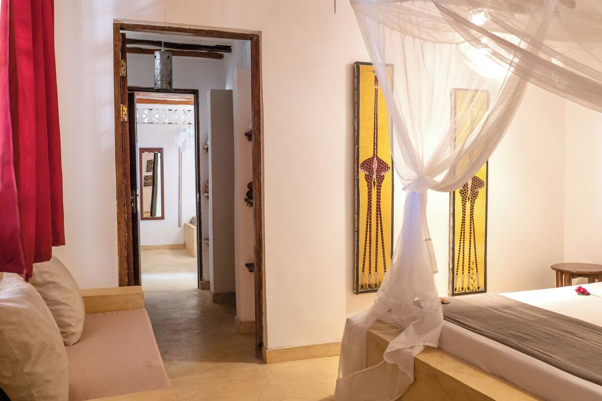 Un dormitorio con cama, mesita de noche, espejo y puerta que da a otra habitación.