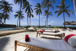 A beachside lounge area with sun loungers, a pool, and palm trees. - Raha Lodge (Jambiani)