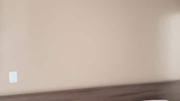 A bedroom with a wooden headboard, a white bed, and a beige wall.
