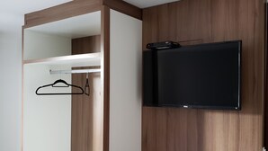 Een moderne kamer met een houten bureau, een aan de muur bevestigde televisie en een kledingkast met een hanggedeelte.