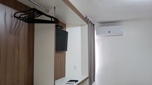 Een hotelkamer met een houten garderobe, een flatscreen televisie aan de muur, een witte nachtkastje met een afstandsbediening, en een airconditioner in het plafond.