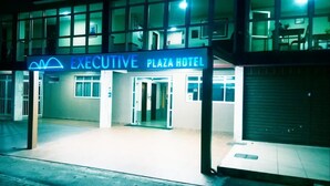 Het uiterlijk van het Executive Plaza Hotel, met een opvallend verlicht bord, een hekpoort en een gesloten luik aan de rechterkant.