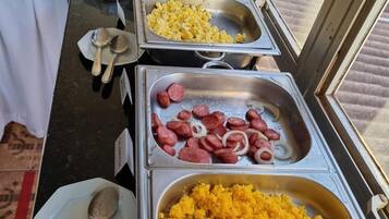 A buffet with various food items including scrambled eggs, sausages, and yellow rice.