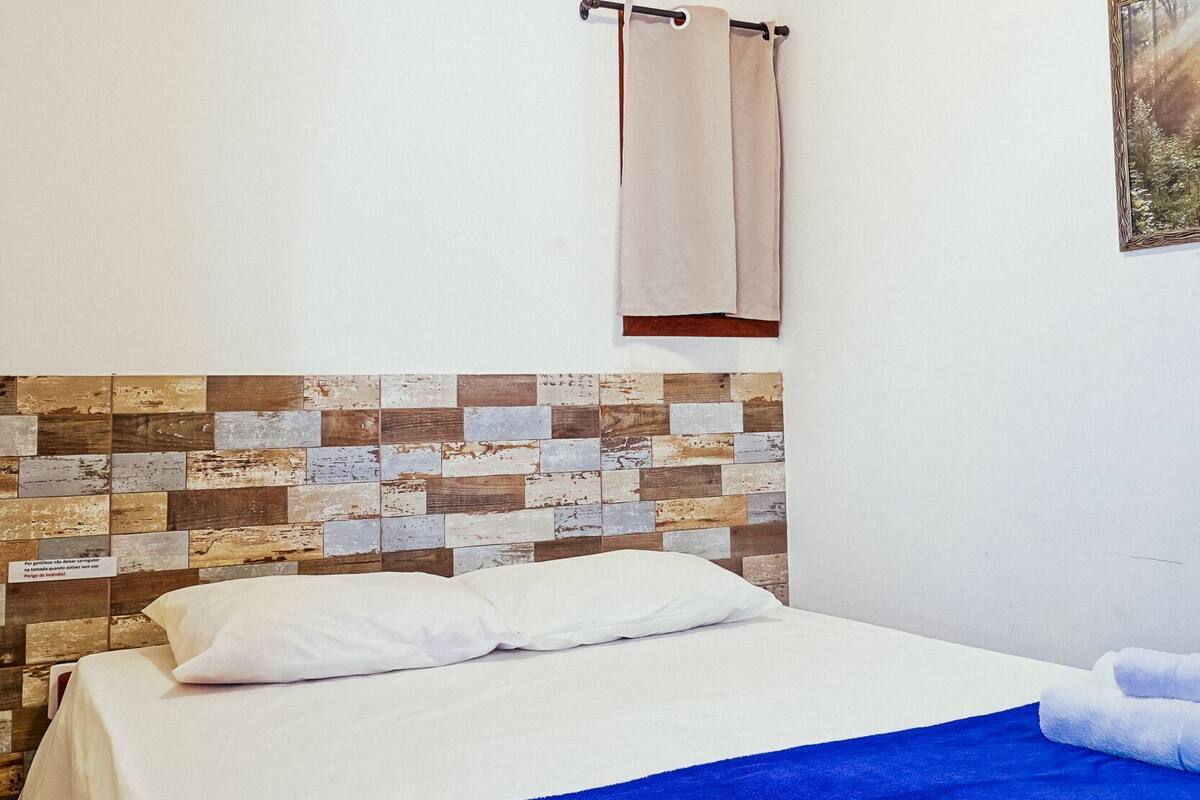 A bedroom with a bed, a ceiling fan, an air conditioning unit, a towel, and a wall-mounted picture.
