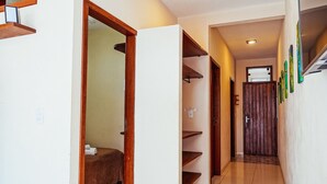 Corredor de hotel com uma cama, uma porta de madeira e uma parede branca com um aviso.