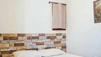 Un dormitorio con cama, ventilador de techo, aire acondicionado, toalla y un cuadro colgado en la pared.