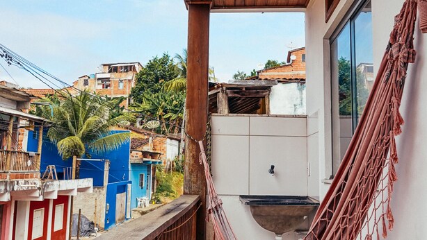 Uma varanda com uma rede, vista do bairro e teto de madeira.