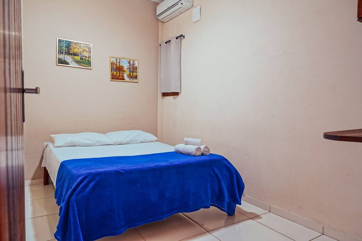 A room with a bed, two wall-mounted paintings, a towel on the bed, and a towel rack.