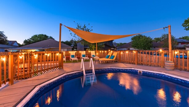 A swimming pool with a wooden deck, lounge chairs, and string lights.