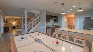 A spacious living area with a foosball table, a kitchen with a granite countertop, and a staircase leading to another level.