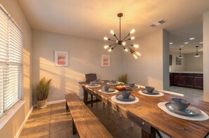 A dining area with a long wooden table, multiple chairs, and a modern chandelier.