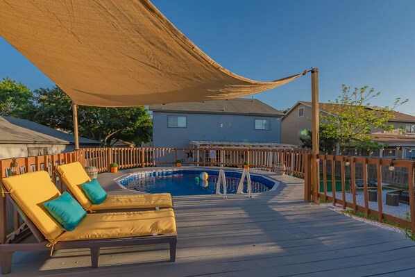 Patio con piscina, terraza de madera y sillas de descanso.