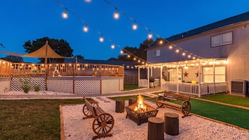 Ein Außenbereich mit Terrasse, Lichterketten, einer Feuerstelle, Holzbänken und einer überdachten Sitzgelegenheit.