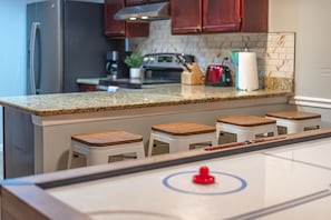 A kitchen with a granite countertop, wooden stools, a stainless steel refrigerator, and a coffee maker.