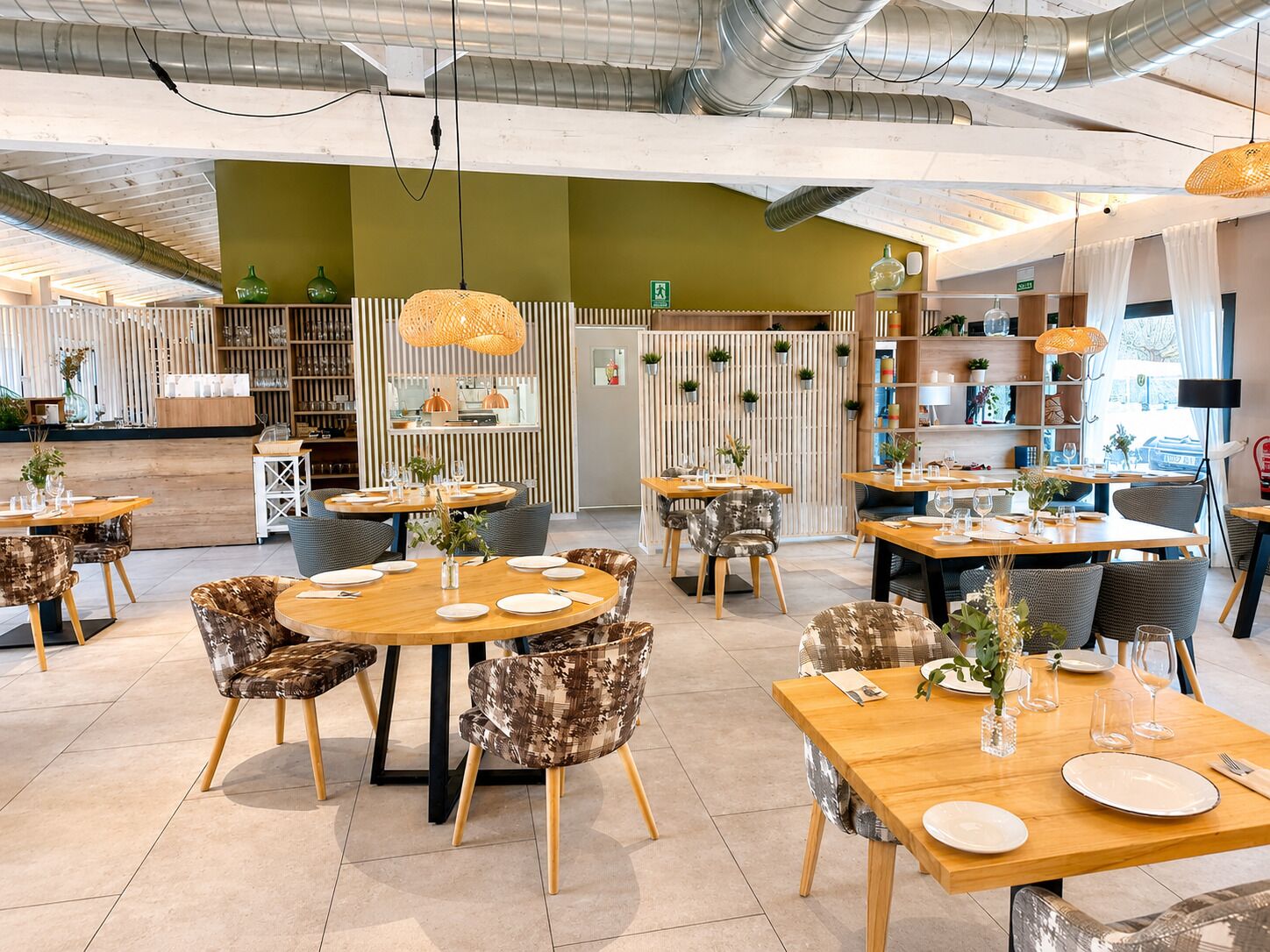 Un interior de restaurante moderno con mesas redondas, sillas estampadas e iluminación colgante.