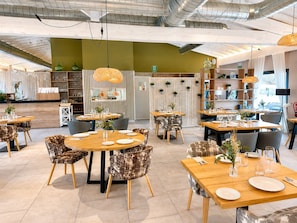A modern restaurant interior with round tables, patterned chairs, and pendant lighting. - Natura Resorts (Casalarreina)