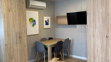 Una sala moderna con una mesa de comedor de madera, sillas grises, un televisor montado en la pared y un armario grande.