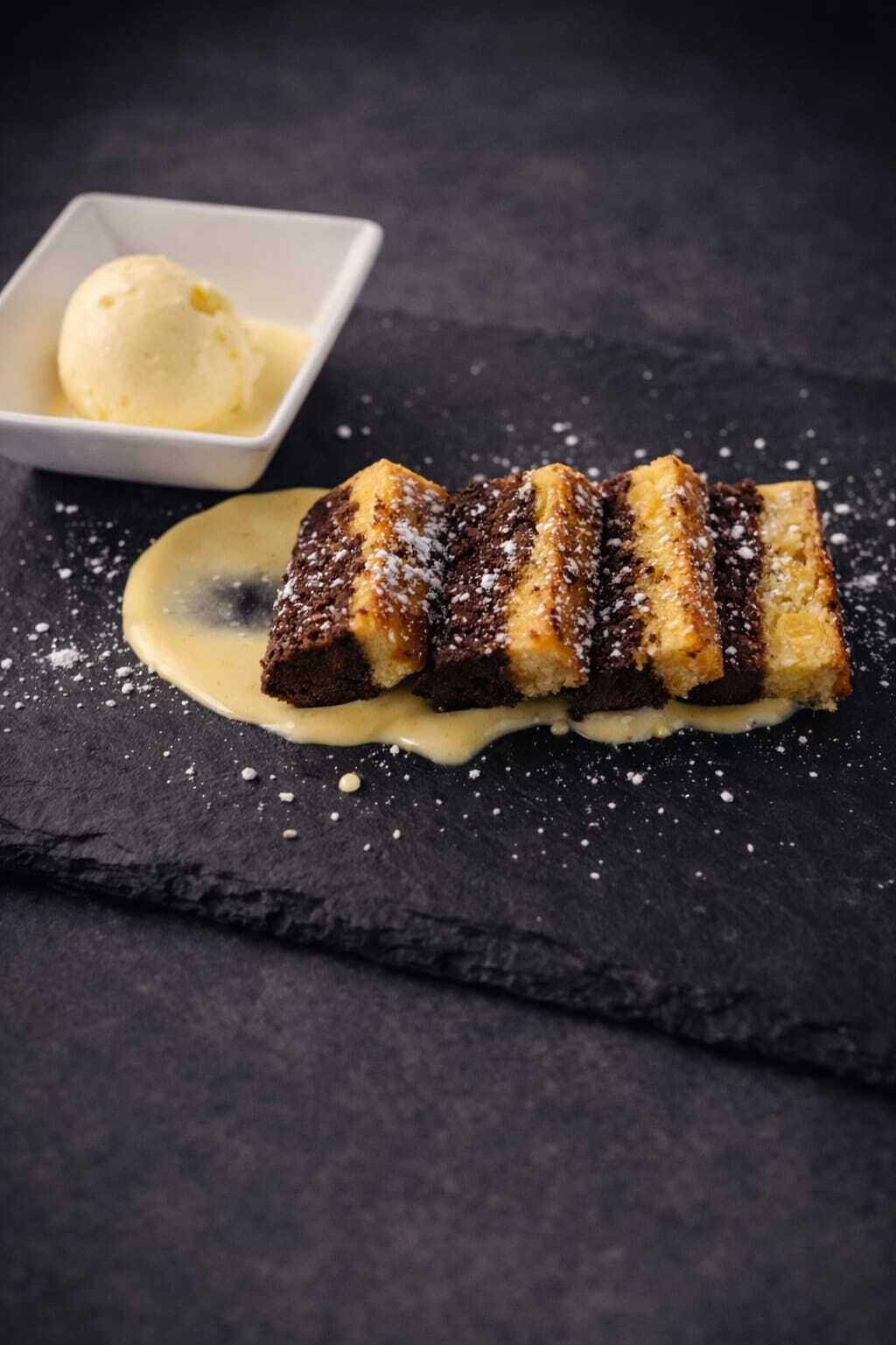 Een dessert met een romige saus en een bol ijs op een leistenen bord.