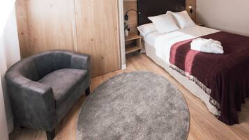 A modern hotel room with a bed, a grey armchair, a round grey rug, and a wooden wardrobe.
