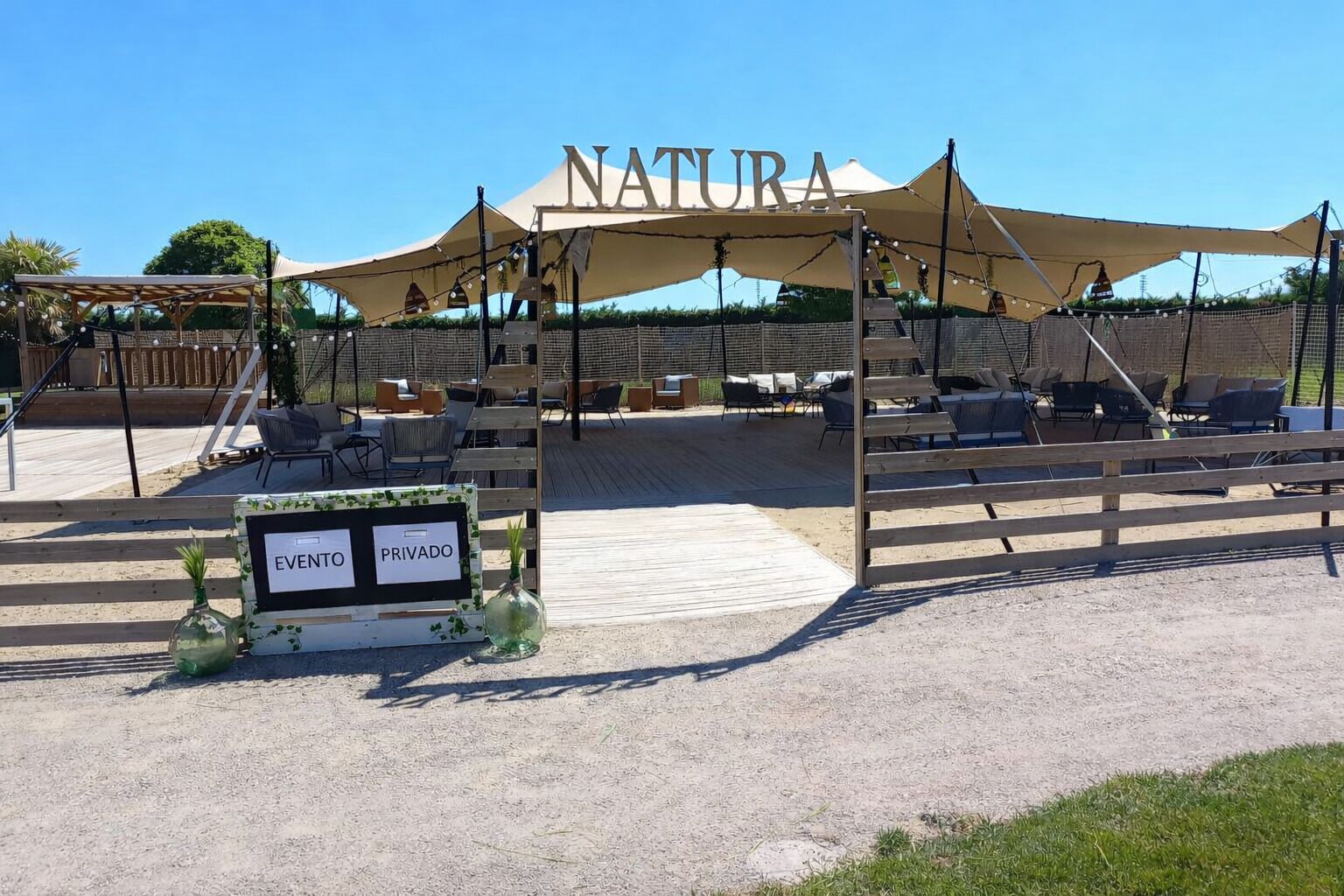 An outdoor seating area with a canopy labeled 'NATURA' and a sign indicating 'EVENTO PRIVADO'.