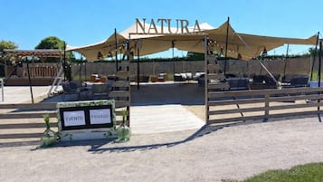 An outdoor seating area with a canopy labeled 'NATURA' and a sign indicating 'EVENTO PRIVADO'.