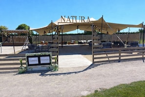 An outdoor seating area with a canopy labeled 'NATURA' and a sign indicating 'EVENTO PRIVADO'.