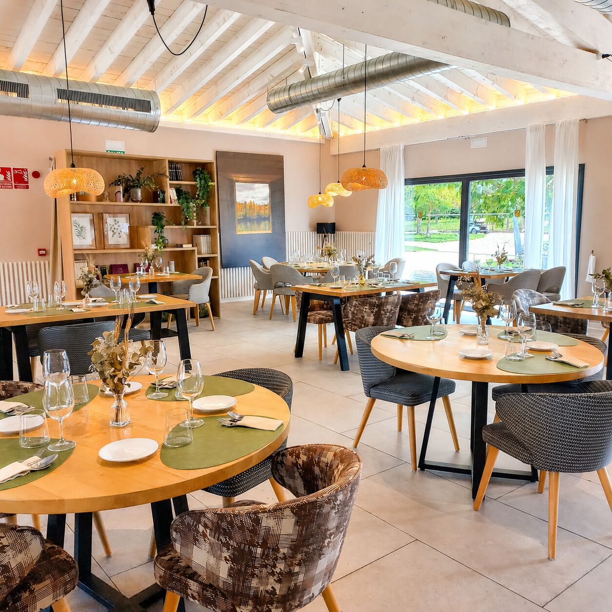 A restaurant with round tables, chairs, and hanging pendant lights.