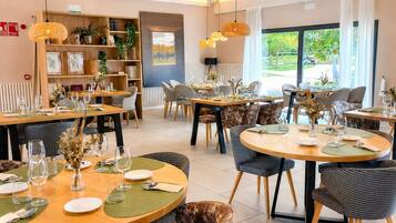 A restaurant with round tables, chairs, and hanging pendant lights.
