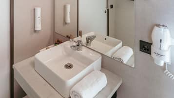 Un baño con lavamanos blanco, espejo, toalla y secador de pelo.