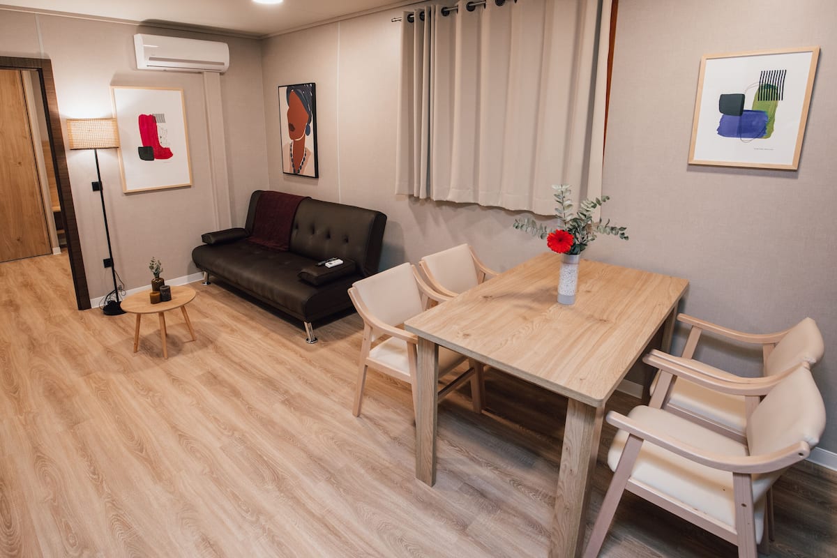 A modern living room with a wooden dining table, two chairs, a sofa, and a floor lamp.
