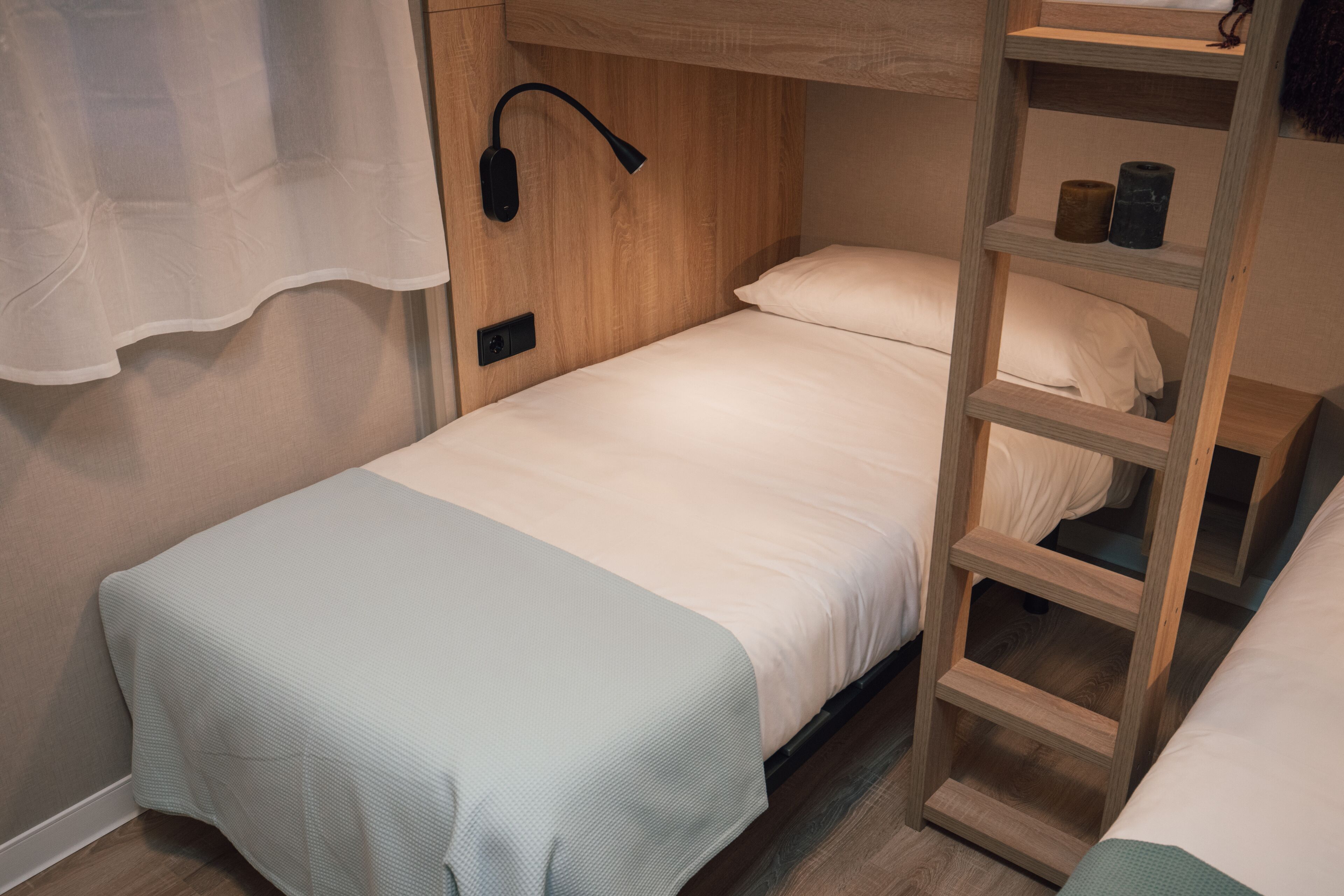 A single bed with a wooden headboard, a bedside lamp, and a shelf with two bottles.
