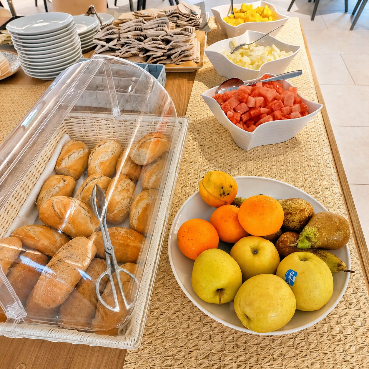 A buffet table with various food items including bread, fruits, and a bowl of watermelon.